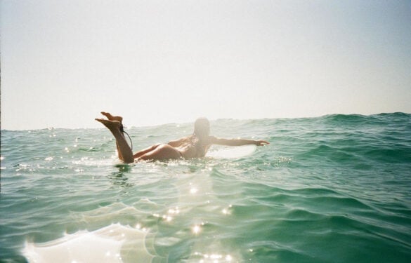 Woman on surfboard paddles out in the sun