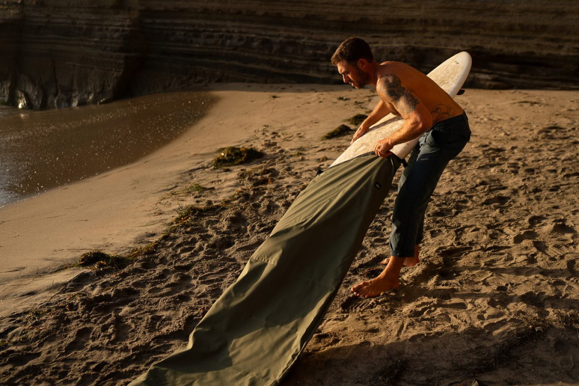 Man putting a surfboard in a boardbag on a beach